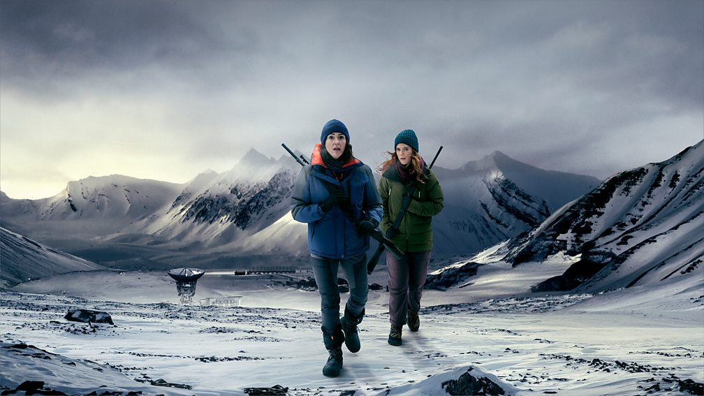 Promotional image for 'Vigil' featuring two characters in warm clothes holding weapons walking across a snowy landscape