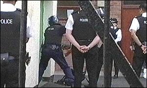 Police officers use a metal battering ram to smash the door in