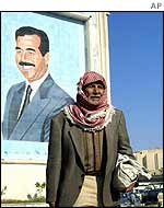 An Iraqi man stands in front of a picture of Saddam Hussein