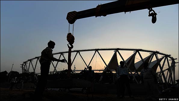 Indian construction workers watch the work of a crane at the Jawahar Lal Nehru Stadium in Delhi