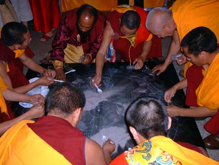 All the monks help to scoop up the coloured sand, now swept into heaps of nondescript grey, using white plastic teaspoons