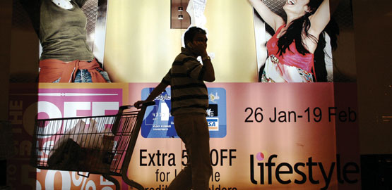Silhouette of a man pulling a shopping trolley while talking on a mobile phone in front of a hoarding advertising a credit card. Picture credit:Reuters