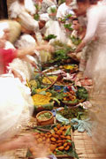 Table full of colourful food served on leaves, surrounded by moving people