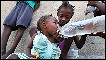 A two year old Haitian girl is given water by her sister