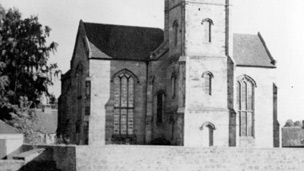 Church with central square tower standing in open fields.
