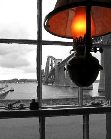 A black and white photo of the view out of a window with an orange coloured lamp in the foreground