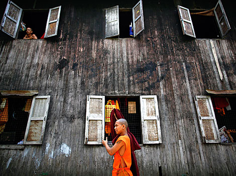 A Buddhist monk carries his robe as another looks out of the window of their monastery.