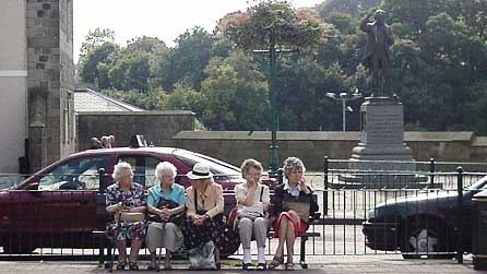 Merched yn eistedd yn y Maes yng Nghaernarfon