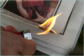 Someone setting fire to the edges of a newspaper