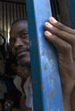 A prisoner peers from behind the bars of a crowded cell