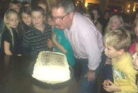 Mr Dyfrig Ellis, Pennaeth Lôn-las a rhai o'r disgyblion yn chwythu'r canhwyllau ar deisen