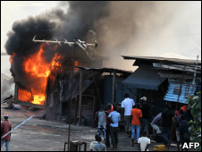 People stand next to stores set on fire during clashes between supporters of Alassane Dramane Ouattara and soldiers of the FDS, loyal to outgoing president Laurent Gbagbo, in the Attecoube neighborhood, in Abidjan
