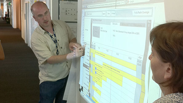 Man stands by wall, explaining a horizontal time chart which has been projected onto it