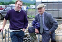 Dau yn pwyso ar rheiliau peniau defaid yn Sioe Meirionnydd