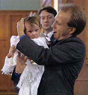 Baby in a white baptismal outfit having water poured on its head