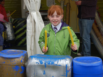 Catrin o Feisgyn yn chwarae'r drymiau ar stondin Asiantaeth yr Amgylchedd.