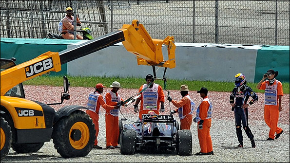 Mark Webber watches as his Red Bull is removed from a gravel trap after an engine failure in Friday practice at the Malaysian Grand Prix