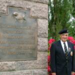 4 June 2004. Pat Kelly, at the 11th Armoured Division Memorial, Flers, Normandy. The Memorial was unveiled by the Division's CO, Major General 'Pip' Roberts in 1974. The sculpture displays the Division's insignia of 'The Black Bull'. The Division charged from Normandy to the Baltic.