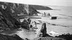 Black and white view looking down from cliffs to small harbour with buildings at Cove.