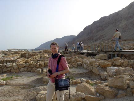 Norman Winter stands among the low stone walls. In the background, a wooden walkway connects various sites within the excavations