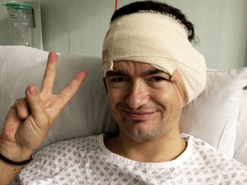 William with his head bandaged, in a hospital bed