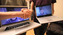 Two men holding laptops, while shaking hands 
