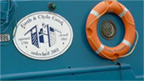 Side of a blue barge with an orange lifebelt and a plaque stating Forth and Clyde canal. Unlocked 2001.