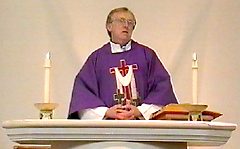 A Christian priest dressed in special robes, standing at an altar with lit candles and reading from a Bible