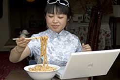 Girl eating noodles while using a laptop