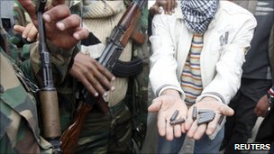 Photo showing soldiers carring guns next to a person holding out their hands full of bullets