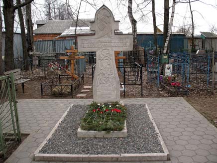 Father Alexander's grave in Novaya Derevnya churchyard, a neat, well-kept stone monument shaped like a Christian cross, with flowers laid on it