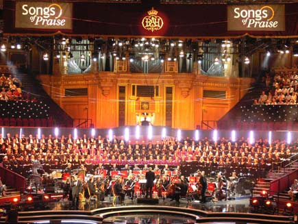 Choirs and orchestra on stage, arranged in a semicircle around the conductor. Audience members can be seen in the galleries high up on either side