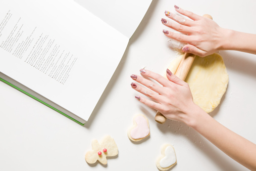 Woman rolling out biscuits following a cookbook.