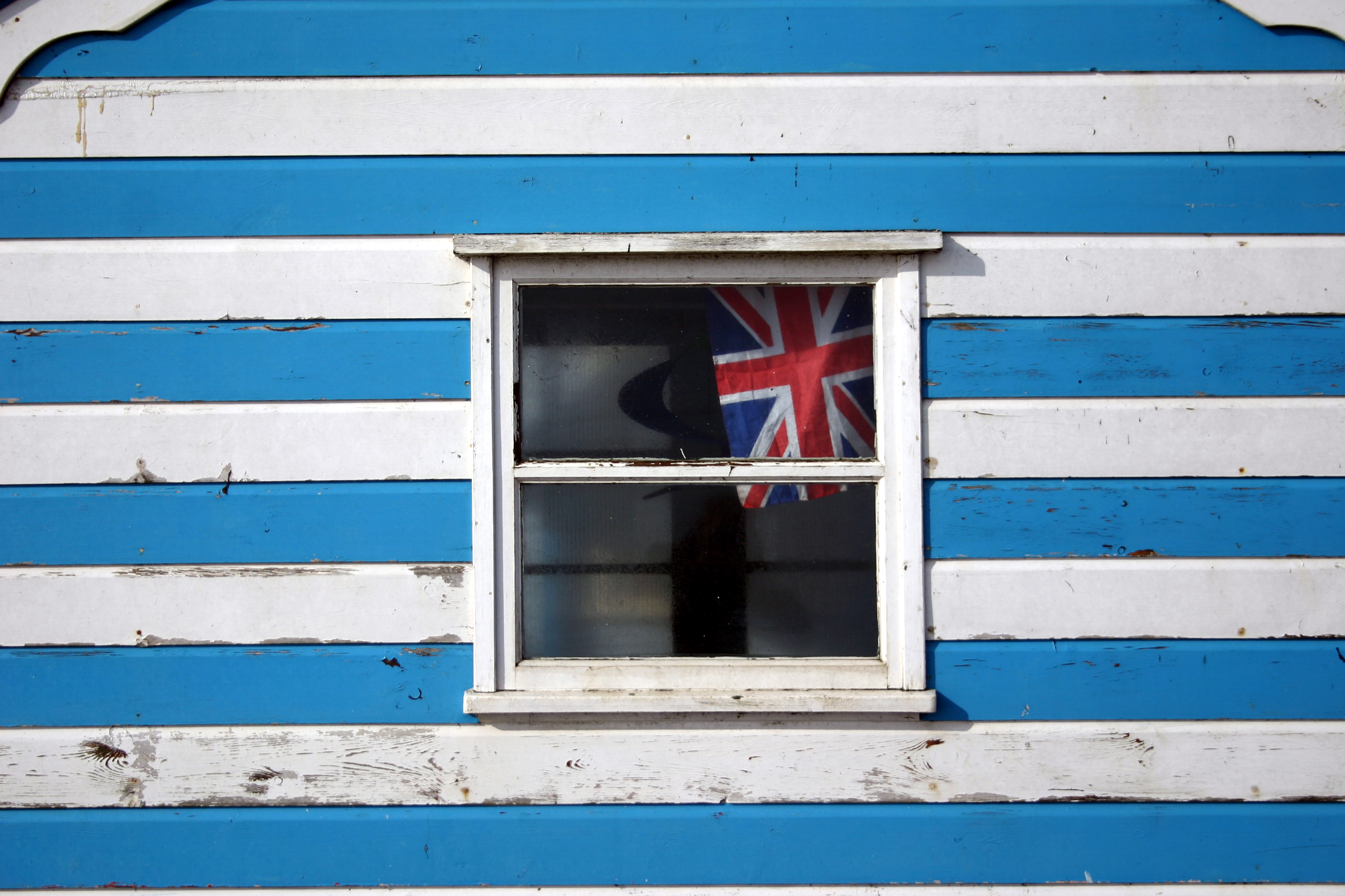 A close-up of a blue and white beach hut with a union jack in the window