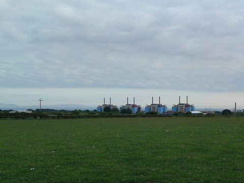 Colour view across fields to four small, squarish towers that are the remains of a power station.