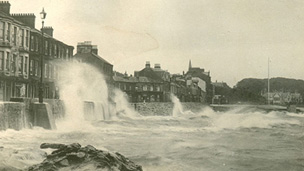 Black and white view of Stuart Street, Millport showing large storm waves breaching the sea wall.