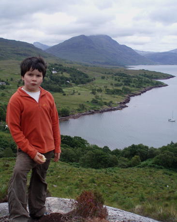 Young boy on a mountain with yacht and loch in distance