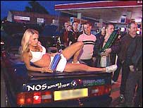 Group of people gathered around a woman laid on a car