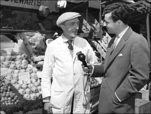 BBC Türkçe yapımcısı Özcan Ergüder, Londra'daki Soho pazarında bir manav ile mülakat yapıyor. İki Şehir programının o ayki bölümü Londra'nın Batısı ve İstanbul'un Avrupa yakasını buluşturuyordu. 14/06/1956 © BBC