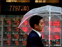 Một người đàn ông đi ngang biển báo cổ phiếu giảm ở Tokyo