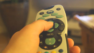 Close-up of Charlie's hand pointing the remote control at the TV