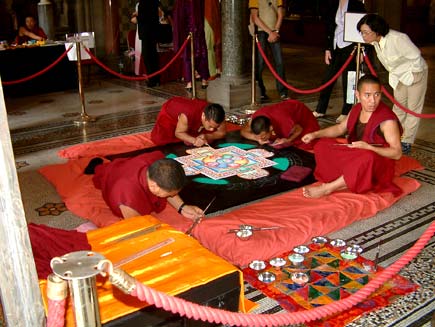 A woman peeks over the shoulder of one of the monks. They are working in a cordoned-off area inside Manchester Town Hall, attracting one or two spectators