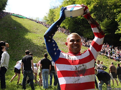 A man holds a large wheel of cheese during a cheese-rolling competition