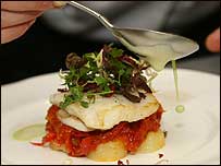 A fish dish being drizzled in sauce.