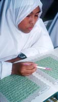 A girl wearing a white gown and Muslim headscarf and digital watch reads the Qur'an