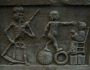 Carving showing the figure of death, a man standing on two hoops and a figure on a throne