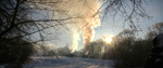 A countryside scene with snow on the ground and clouds of smoke from a building where charcoal is being burned