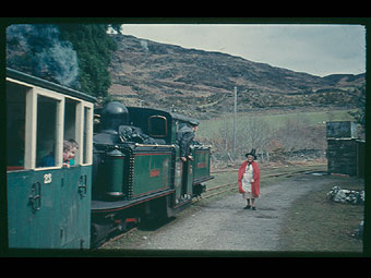 Tren a dynes mewn gwisg Gymreig mewn gorsaf