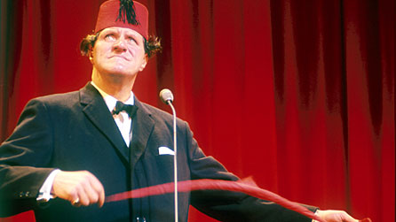 Image of Tommy Cooper, wearing his trademark fez, performing a magic trick.