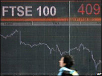 Woman walks past display screen of FTSE 100 index